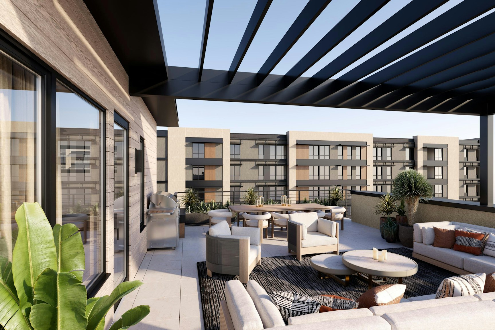A modern rooftop patio with comfortable seating, a grill, and a pergola. The space features plants and lounge areas, overlooking contemporary buildings nearby.